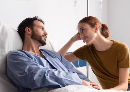 Un hombre joven con barba y un pijama, en una cama de hospital comparte mirada con una joven que le coge la mano