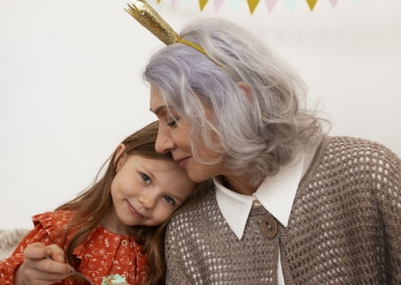 Una mujer de pelo canoso con una chaqueta de punto junto a una niña, con un vestido de flores, que apoya su cabeza sobre su hombro